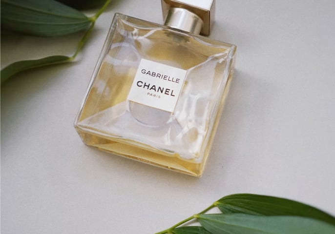 Picture of Gabrielle Essence Eau De Parfum laying down flat on a table surrounded by green leaves